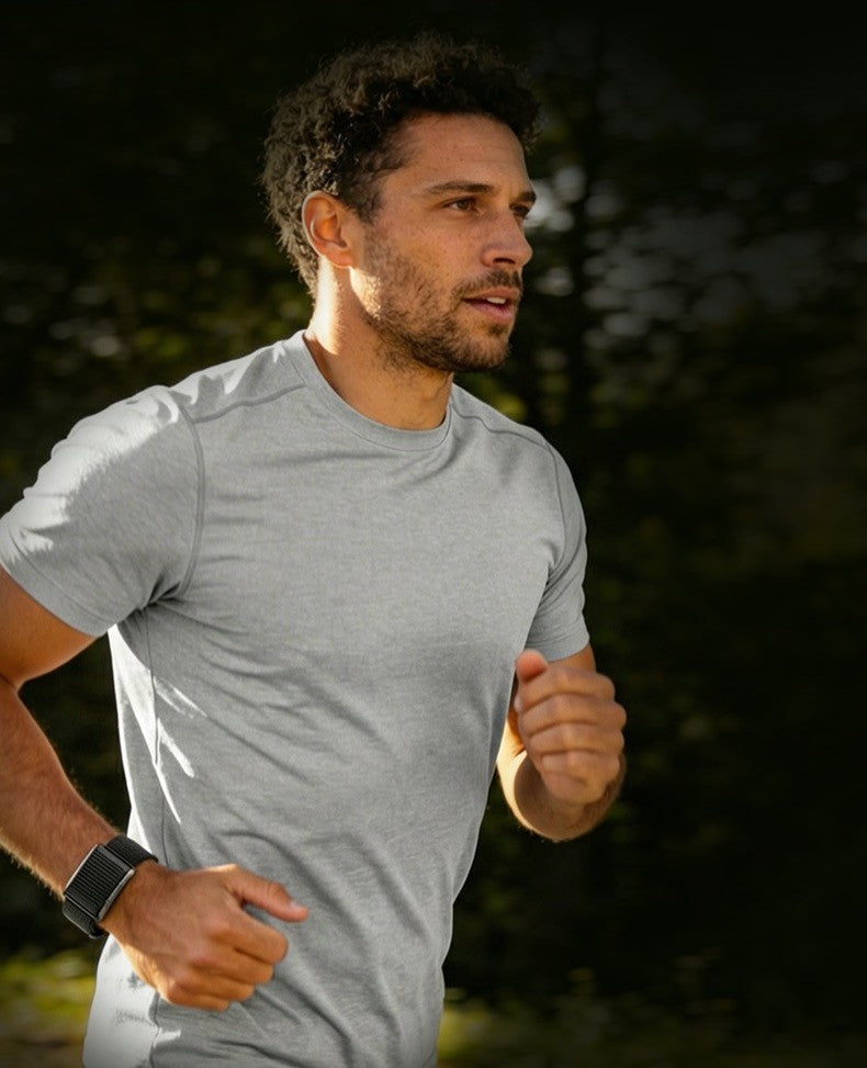 A man jogging outdoors wearing a light gray heathered short-sleeve athletic t-shirt and a black smartwatch.